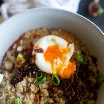 Savory Asian Oatmeal topped with crispy beef, chilli oil, spring onions and poached egg in a white bowl.